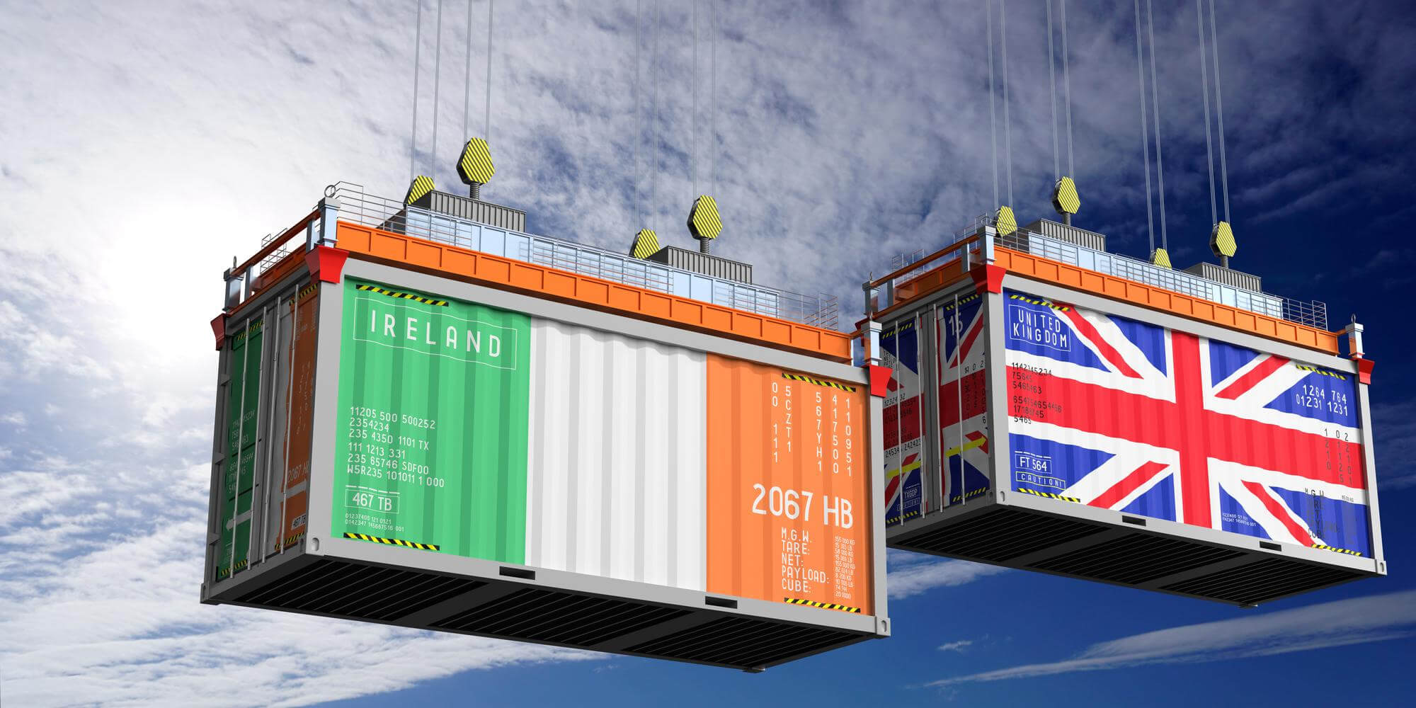 Two large shipping containers, one decorated with the flag of Ireland and the other with the Union Jack of the United Kingdom, are suspended by cranes against a blue sky.