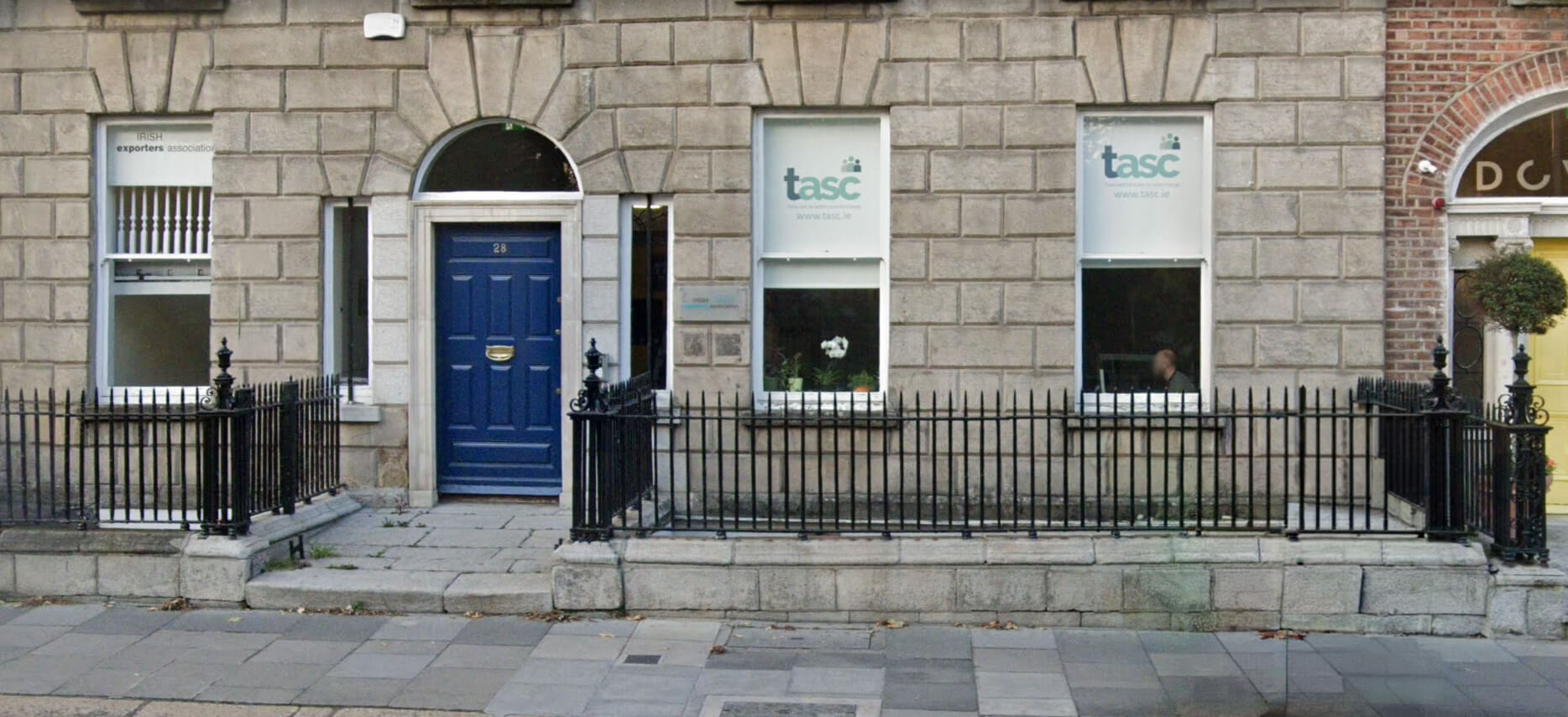 The front of a stone Georgian-style building with a navy blue door and windows displaying signs for TASC and the Irish Exporters Association.